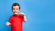 Smiling boy with healthy teeth brushing his teeth with a toothbrush on a blue isolated background. Oral hygiene. A place for your text.