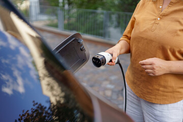 Wall Mural - Woman holding power supply cable at electric vehicle charging station, closeup