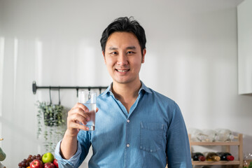 Wall Mural - Portrait of Asian young man drinking glass of milk in kitchen at home.