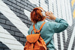 © okrasiuk - Back view stylish woman in bright clothes wearing wireless headphones on her head and listening to music while walking near city urban painted wall. Fashionable hipster lifestyle. Selective focus.