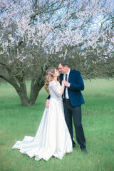  The bride and groom with blond long hair in a white dress in a spring garden near a flowering tree. Emotions and feelings