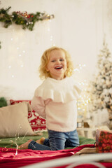 Canvas Print - Cute little toddler curly girl in winter christmas sweater, sitting in cozy room, decorated for christmas