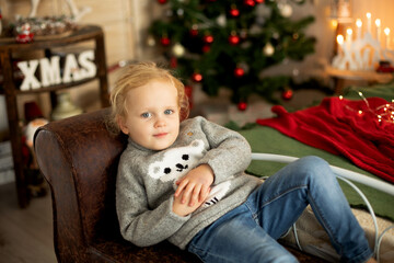 Canvas Print - Cute little toddler curly girl in winter christmas sweater, sitting in cozy room, decorated for christmas