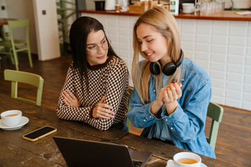 White women in eyeglasses using gadgets while drinking tea in cafe