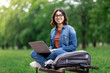 © Prostock-studio - Happy Middle Eastern Female Student Sitting On Bench Outdoors With Laptop