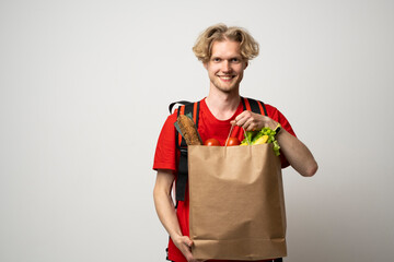 Wall Mural - Portrait of smiling cheerful handsome young delivery man holding grocery shopping bag isolated on white background.