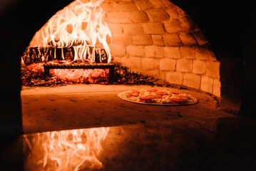 Wall Mural - A cooking and baking pizza in a firewood oven. Pizza Margherita, four cheese or meat pizza into the oven. Italian traditional pizza is cooked in a stone wood-fired oven.