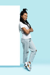 Sticker - Full length of young woman wearing casual clothes smiling and pointing finger at copyspace isolated over blue background