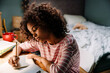 © Drobot Dean - Black curly girl doing homework while sitting at table