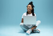 © opolja - Happy young woman sitting on the floor with crossed legs and using laptop on blue background.