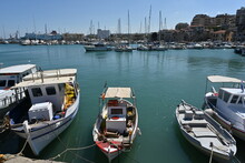 Old Wooden Fishing Boats Moored In Port In  Heraklion Near The City Center.  In Horizon Are Buildings Of The Town And And White Private Luxury Yachts. Und Blue Sky.