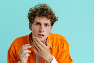 Wall Mural - Young handsome serious curly man in shirt touching his cheek