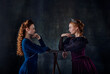 Portrait of two beautiful women in image of queens isolated over dark background. Confrontation, eye to eye