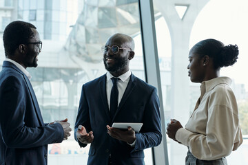 Poster - Group of three young African American employees in formalwear having discussion of ideas while preparing new business project