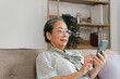 © NanSan - Relaxed asian mature 60s years old woman using smartphone, texting message at home.
