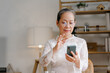Relaxed asian mature 60s years old woman using smartphone, texting message at home.
