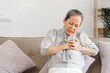© NanSan - Senior asian mature woman heart disease, sitting on couch.