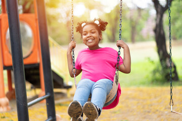 Wall Mural - Smiling African American child girl playing on swing at the playground. Happy girl having fun on swing outdoor