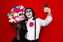 Photo Of Creepy Couple Man Lady Cuddle Hold Telephone Make Selfie Video Call Friend Wear Black Dress Death Costume Mask Sugar Skull Roses Headband Suspenders Isolated Red Color Background