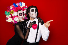 Photo Of Two People Zombie Scary Man Lady Cuddle Direct Finger Look Empty Space Excited Neighbors Decor Wear Black Dress Death Costume Roses Headband Suspenders Isolated Red Color Background