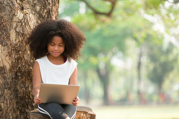 Wall Mural - Happy African American child girl using laptop computer outdoors in the park. Kid girl learning outside at the school