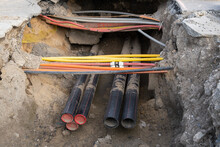 Network Cables In Red Corrugated Pipe Are Buried Underground On The Street. Underground Electric Cable Infrastructure Installation. Construction Site With A Lot Of Communication Cables