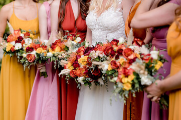 Bride and Bridesmaids in autumn colors holding colorful bouquets filled with orange roses and yellow anemones, close up crop no faces