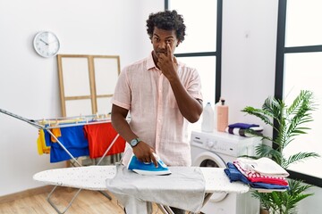 Canvas Print - African man with curly hair ironing clothes at home pointing to the eye watching you gesture, suspicious expression