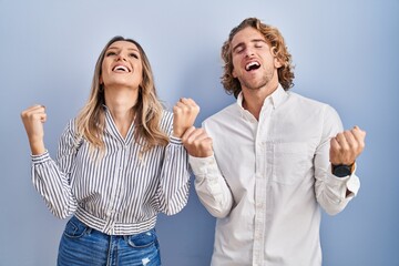 Canvas Print - Young couple standing over blue background celebrating surprised and amazed for success with arms raised and eyes closed. winner concept.