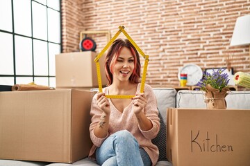 Poster - Young caucasian woman sitting on the sofa at new home winking looking at the camera with sexy expression, cheerful and happy face.