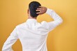 © Krakenimages.com - Young hispanic man standing over yellow background backwards thinking about doubt with hand on head