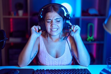 Sticker - Young blonde woman playing video games wearing headphones covering ears with fingers with annoyed expression for the noise of loud music. deaf concept.