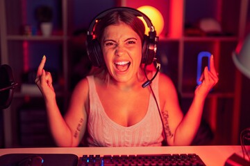 Canvas Print - Young blonde woman playing video games wearing headphones shouting with crazy expression doing rock symbol with hands up. music star. heavy concept.