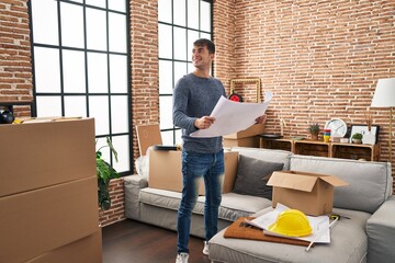 Sticker - Young hispanic man smiling confident reading house plans at new home