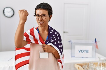 Canvas Print - Young hispanic woman with short hair at political campaign election holding usa flag annoyed and frustrated shouting with anger, yelling crazy with anger and hand raised