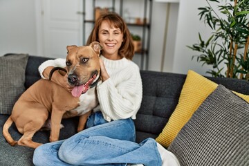 Poster - Young caucasian woman smiling confident hugging dog sitting on sofa at home