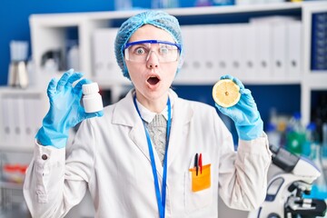 Poster - Beautiful woman working at scientist laboratory holding pills and lemon afraid and shocked with surprise and amazed expression, fear and excited face.