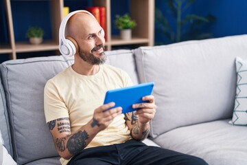 Canvas Print - Young bald man watching video on touchpad sitting on sofa at home