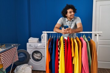 Sticker - Young hispanic man using smartphone leaning on rack at laundry room