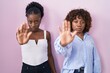 © Krakenimages.com - Two african women standing over pink background doing stop sing with palm of the hand. warning expression with negative and serious gesture on the face.
