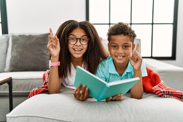 Canvas Print - Two siblings lying on the sofa reading a book smiling amazed and surprised and pointing up with fingers and raised arms.