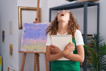 Sticker - Young caucasian woman holding art notebook angry and mad screaming frustrated and furious, shouting with anger looking up.