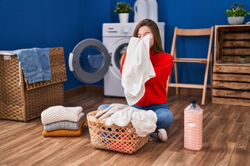 Wall Mural - Young blonde woman smelling clothes sitting on floor at laundry room