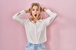 © Krakenimages.com - Young caucasian woman wearing casual white shirt over pink background crazy and scared with hands on head, afraid and surprised of shock with open mouth