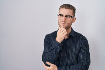 Poster - Young caucasian man standing over isolated background with hand on chin thinking about question, pensive expression. smiling with thoughtful face. doubt concept.