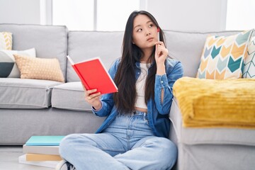 Canvas Print - Young chinese woman reading book with doubt expression at home