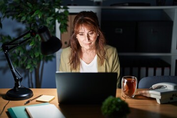 Sticker - Middle age hispanic woman working using computer laptop at night relaxed with serious expression on face. simple and natural looking at the camera.