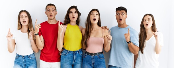 Canvas Print - Group of people wearing casual clothes standing over isolated background amazed and surprised looking up and pointing with fingers and raised arms.