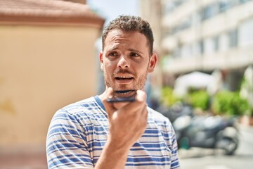 Wall Mural - Young hispanic man talking on the smartphone at street