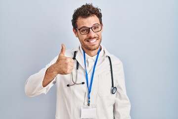 Sticker - Young hispanic man wearing doctor uniform and stethoscope doing happy thumbs up gesture with hand. approving expression looking at the camera showing success.